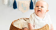 Arnie is registered to the contest to win money with this photo: baby, banner, basket, celebration, child, cute, decor, face, half_year, happy, indoor, infant, milestone, portrait, sitting, smiling, studio_photo, tassel_garland, white_clothing, woven