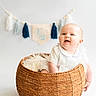 baby, basket, smiling, tassel_garland, banner, half_year, celebration, white_clothing, cute, infant, studio_photo, happy, portrait, child, indoor, decor, face, sitting, woven, milestone