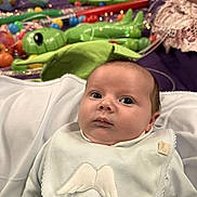 Arnie is registered to the contest to win money with this photo: baby, infant, bib, angel_wings, toys, green_aliens, balls, purple_blanket, face, person, child, clothing, soft_focus, curious, indoors, cute, portrait, newborn, lying_down, background