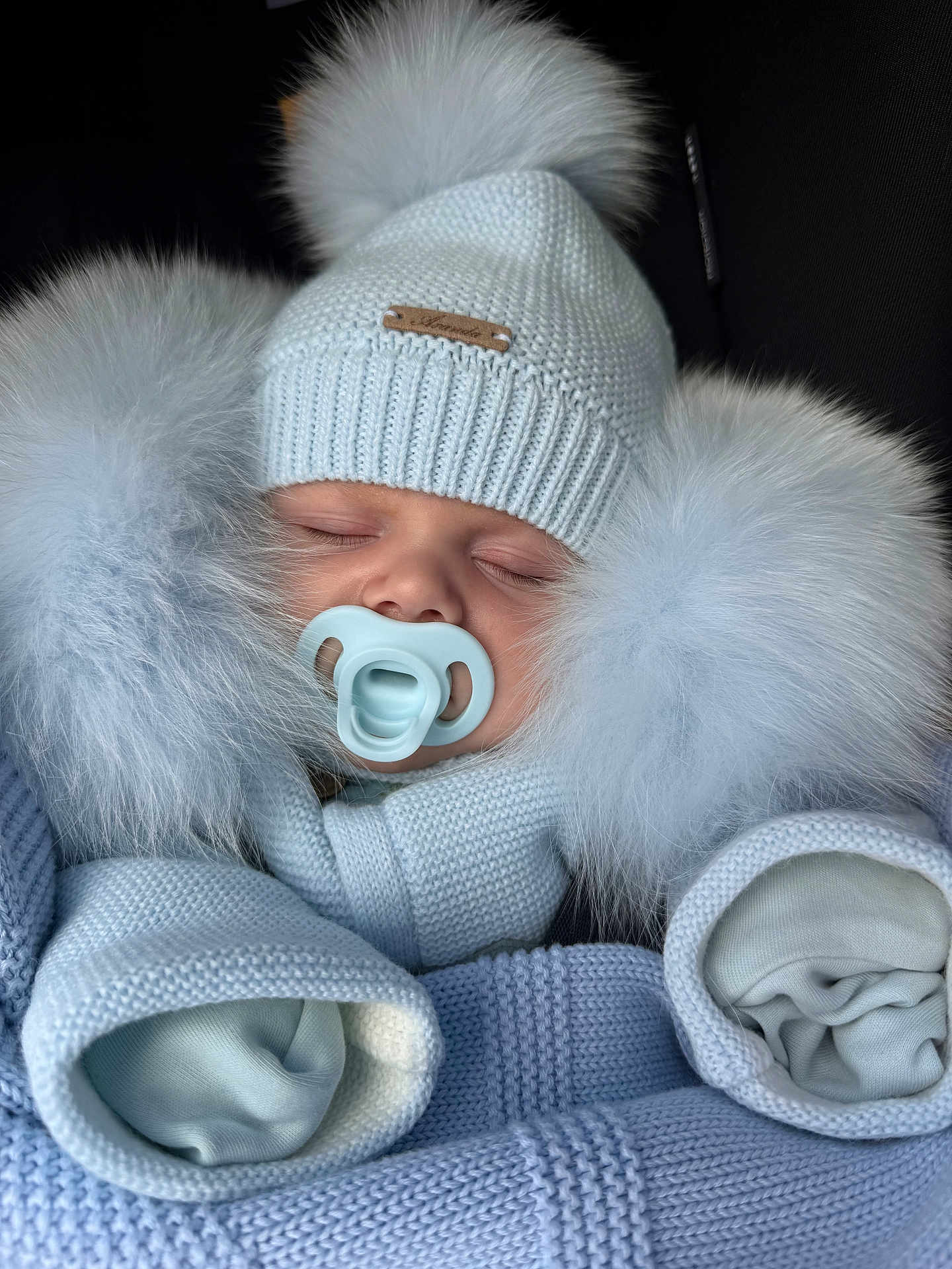 Arnie is registered to the contest to win money with this photo: baby, sleeping, pacifier, hat, knitwear, pom_poms, blue, winter, cozy, bundle, infant, face, closed_eyes, cute, warm, soft, child, portrait, clothing, hands_covered
