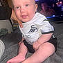 Leo is registered to the contest to win money with this photo: baby, child, smiling, sitting, clothing, jersey, person, hand, blanket, foot, toes, face, head, indoor, television, blurred_background, home, casual, supporting_hand, cute