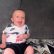 Leo is registered to the contest to win money with this photo: baby, smiling, happy, infant, child, sitting, couch, blanket, clothing, nike, shorts, tshirt, indoor, face, person, legs, hand, pattern, fabric, cute