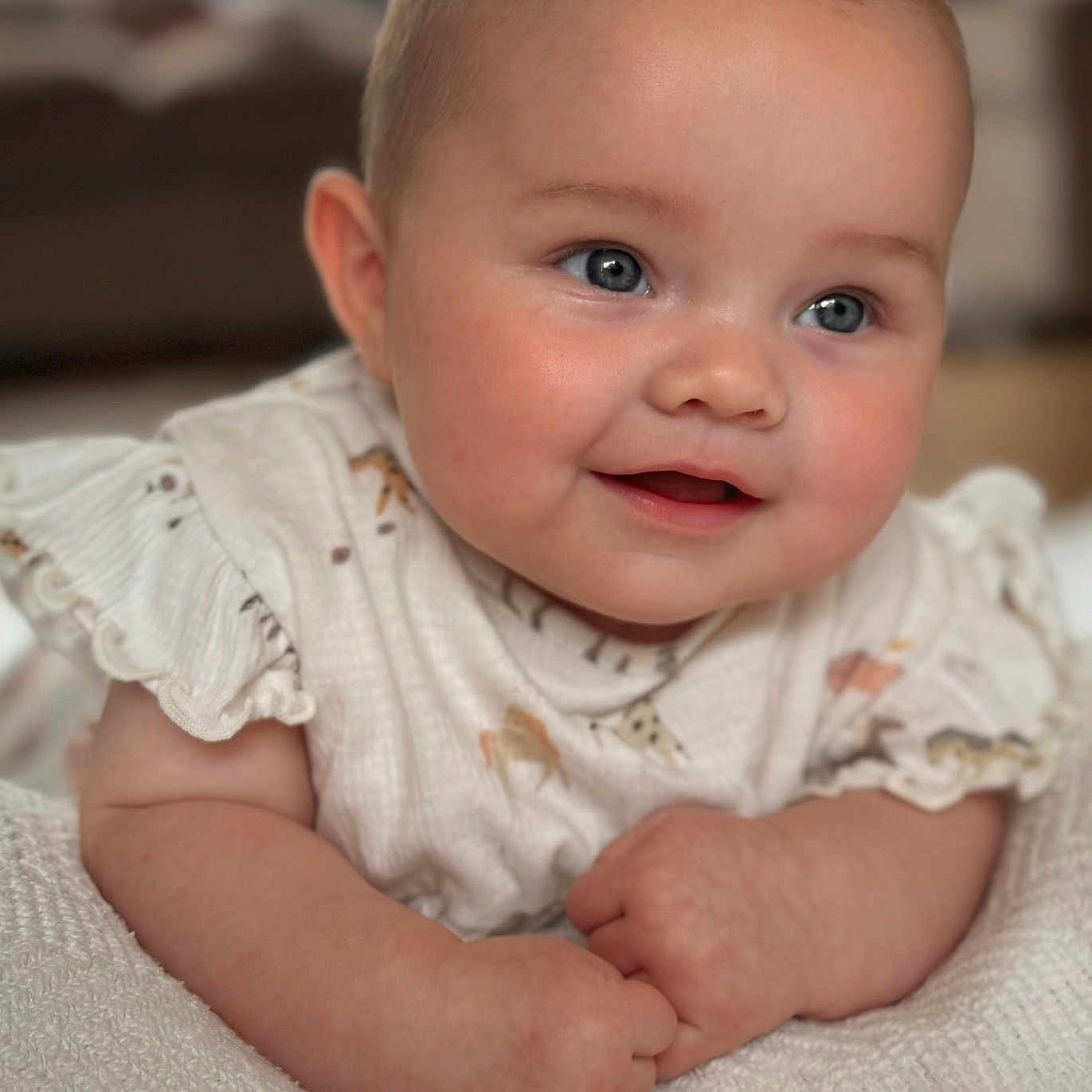 Florence is registered to the contest to win money with this photo: animal_print, baby, blue_eyes, child, close_up, cute, expression, hands, happy, indoors, infant, portrait, resting, rosy_cheeks, ruffled_sleeves, skin, smile, soft_focus, warm_lighting, white_blanket