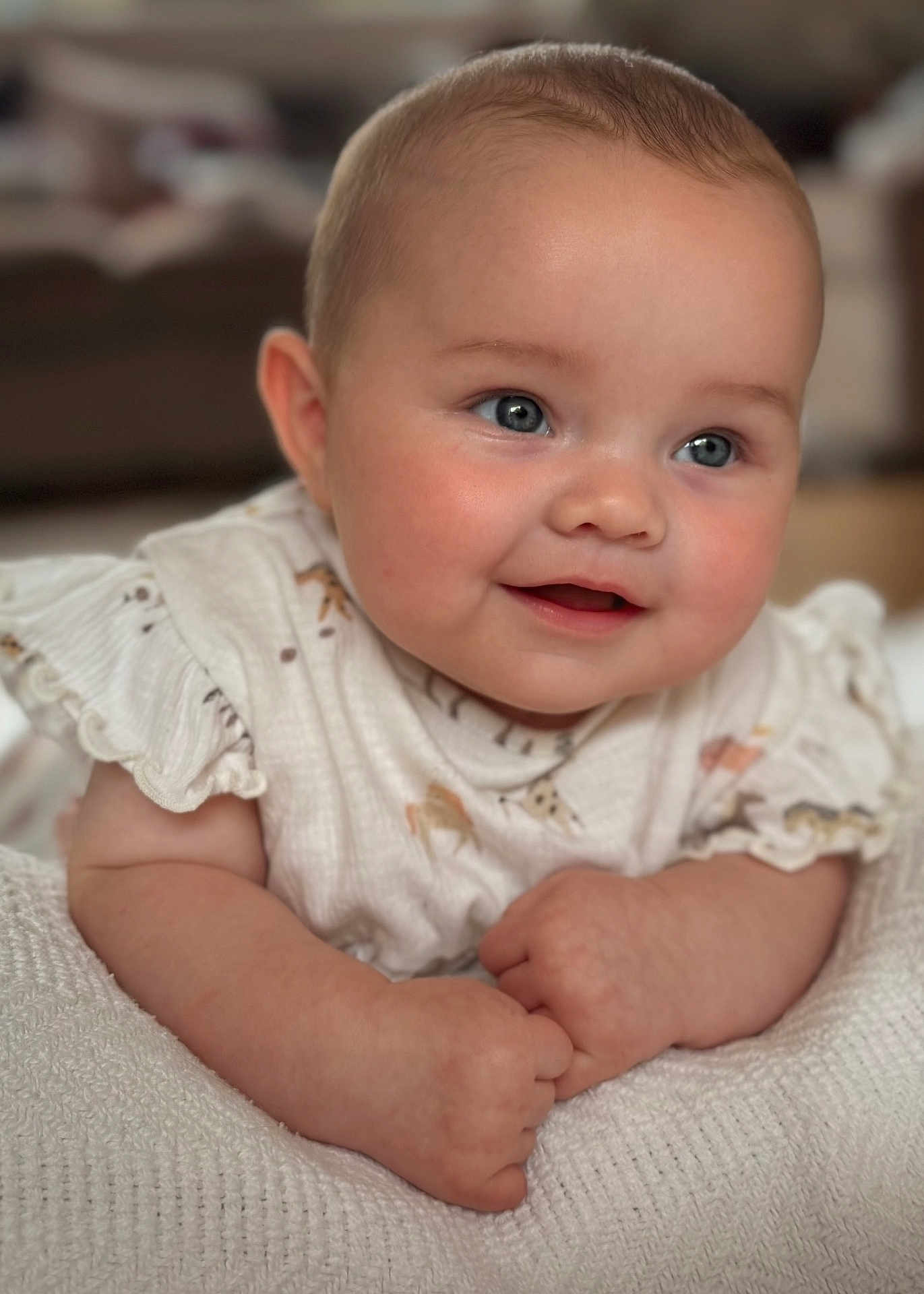 Florence is registered to the contest to win money with this photo: baby, infant, smile, blue_eyes, rosy_cheeks, white_blanket, ruffled_sleeves, animal_print, soft_focus, close_up, cute, portrait, child, resting, indoors, warm_lighting, happy, skin, hands, expression