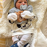 Lyam participe au concours pour gagner de l'argent avec cette photo : baby, pacifier, beanie, blanket, clothing, footwear, infant, person, cute, soft, warm, sleepwear, toy, animal_print, mittens, laying_down, indoor, newborn, comfort