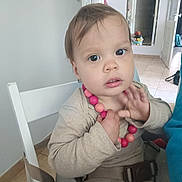 Rita a rejoint le concours — aidez-le/la à gagner de superbes lots ! chair, child, clothing, curious, expression, eyes, face, floor, hair, hands, high_chair, home, indoor, mirror, necklace, person, pink_beads, seat_belt, tile, toddler