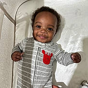 Kayceon is registered to the contest to win money with this photo: baby, smiling, crib, onesie, gray_stripes, red_crab_patch, hand, infant, cute, child, happy, face, person, sleeping_area, fabric, bed, indoors, young, portrait, closeup