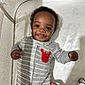baby, smiling, crib, onesie, gray_stripes, red_crab_patch, hand, infant, cute, child, happy, face, person, sleeping_area, fabric, bed, indoors, young, portrait, closeup