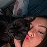 person, cat, black_cat, face, pillow, blanket, bedroom, curtains, indoor, night, close_up, snuggling, affection, cozy, sleepwear, hair, skin, hand, facial_expression, rest