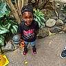 child, boy, cap, toy_car, black_tshirt, miles_morales, sneakers, shorts, plants, rocks, bird, outdoor, smiling, concrete_floor, backpack, yellow_cone, greenery, nature, happy, portrait