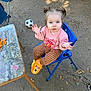 Haisley is registered to the contest to win money with this photo: toddler, child, outdoor, blue_chair, pink_sweatshirt, striped_pants, tigger_slippers, soccer_ball, scooter, table, snacks, curious_expression, pigtails, face, hands, concrete_ground, leaves, sunlight, shadow, person
