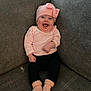 baby, smiling, pink_hat, pink_socks, striped_shirt, black_pants, couch, gray_couch, happy, infant, child, seated, indoors, cute, portrait, cozy, clothing, person, face, headwear