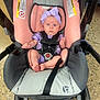 baby, infant, stroller, car_seat, headband, purple_clothing, pink, gray, baby_seat, floor, infant_clothing, baby_babywear, child, toddler, baby_face, baby_feet, baby_hands, indoor, person, seatbelt
