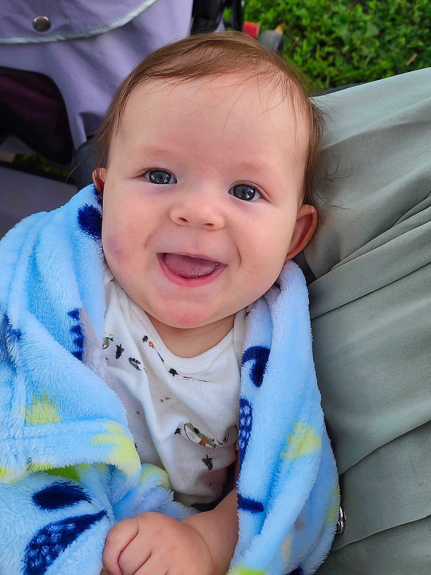 Camden is registered to the contest to win money with this photo: baby, child, smiling, blanket, blue_blanket, stroller, happy, face, cute, infant, clothing, outdoor, nature, person, portrait, small_hand, soft_texture, head, cheerful, eyes