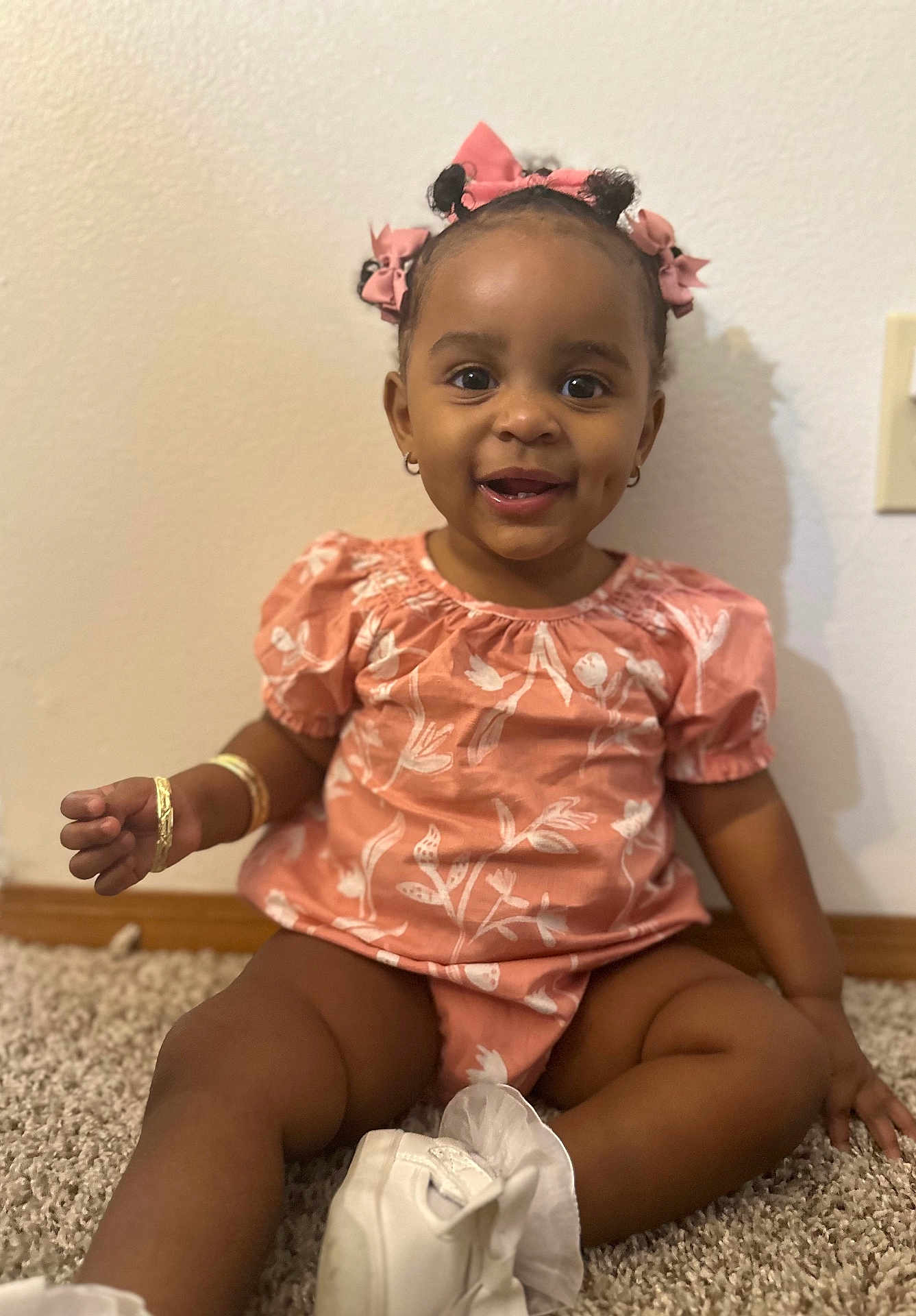 Jahlori is registered to the contest to win money with this photo: toddler, child, smiling, pink_bows, floral_outfit, carpet, sitting, happy, indoor, cute, person, footwear, bracelet, earrings, skin, hair, baby, portrait, young_child, joy