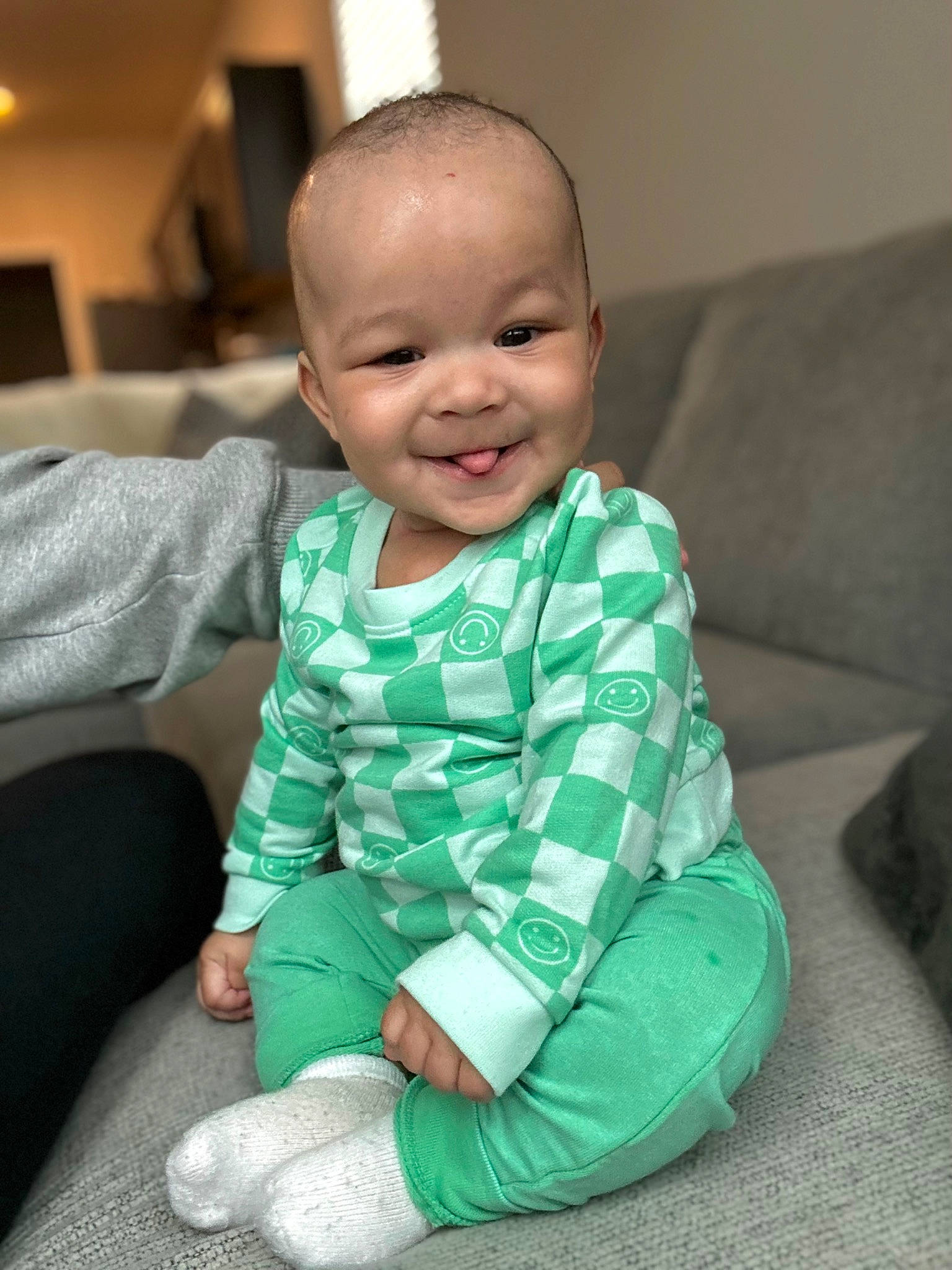 Kaiser is registered to the contest to win money with this photo: baby, baby_toddler_clothing, cheek, child, comfort, couch, eye, flooring, foot, fun, happy, human_leg, joy, laugh, person, room, sitting, skin, sleeve, smile