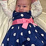baby, blanket, crib, cute, diaper_pack, face, hands_up, home_interior, huggies_pack, infant, long_sleeve, lying_down, newborn, pink_bow, polka_dot_dress, portrait, rosy_cheeks, smiling, soft_toy, tights