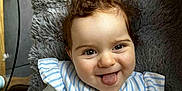 Cassandre a rejoint le concours — aidez-le/la à gagner de superbes lots ! baby, child, curly_hair, tongue_out, smiling, striped_clothing, plush_cushion, indoor, hand, face, happy, person, fabric, patterned_cloth, cute, skin, head, sitting, playful, cozy