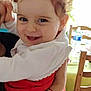 Cassandre a rejoint le concours — aidez-le/la à gagner de superbes lots ! toddler, child, smiling, curly_hair, white_clothing, red_clothing, arm, bracelets, tattoo, indoor, dining_table, chair, water_bottle, plant, window, person, happy, holding, face, home