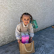 Myla participe au concours pour gagner de l'argent avec cette photo : child, girl, smiling, braids, pigtails, bag, burlap_bag, outdoor, concrete, wall, sunny, happy, clothing, cute, portrait, young, person, casual, daylight, holding