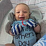 baby, infant, smiling, mittens, blue_onesie, mother's_day, cushioned_seat, patterned_fabric, happy, portrait, indoor, child, face, head, person, young_child, clothing, soft_toys, comfort, celebration