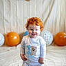Tj is registered to the contest to win money with this photo: child, toddler, red_hair, smiling, onesie, birthday, balloons, banner, indoor, celebration, happy, curly_hair, blue_eyes, standing, plush, carpet, decorations, party, cute, portrait