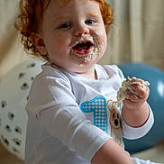 Tj is registered to the contest to win money with this photo: toddler, child, red_hair, cake, birthday, frosting, smiling, balloon, white_clothing, celebration, face, hand, messy, happy, indoors, sitting, cute, party, first_birthday, baby
