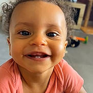 Kélya participe au concours pour gagner de l'argent avec cette photo : child, toddler, smiling, curly_hair, face, teeth, shirt, indoor, living_room, floor, couch, happy, cute, baby, person, portrait, close_up, furniture, home, skin