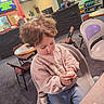 Leah is registered to the contest to win money with this photo: toddler, child, curly_hair, plastic_chair, bowling_alley, bowling_balls, indoor, casual_clothing, jeans, sweatshirt, playing, table, chairs, floor, focused, young_child, seated, person, leisure, activity