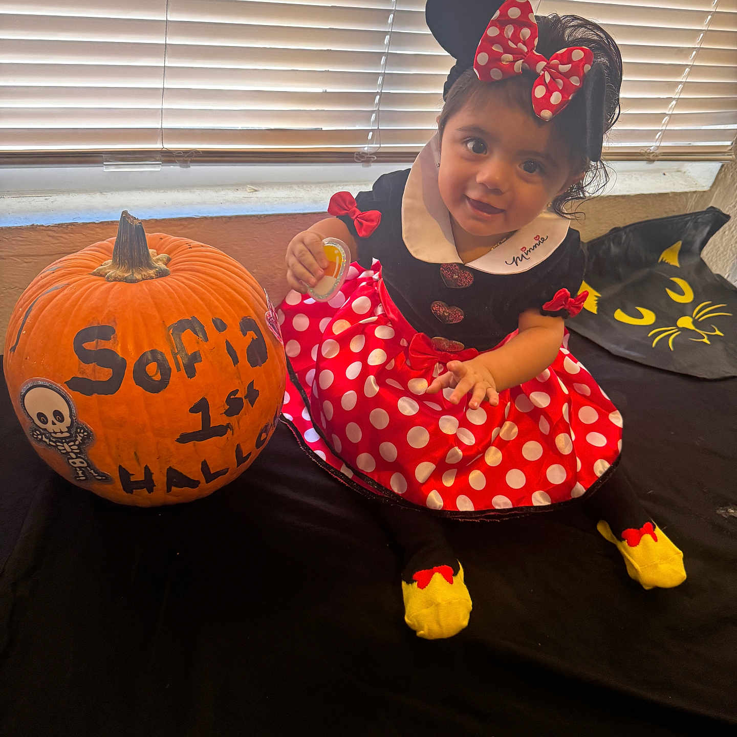 Isa joined the competition — help win amazing prizes! black, black_cat_design, blinds, child, costume, cute, decoration, dress, face, halloween, indoor, minnie_mouse, polka_dots, pumpkin, red, smile, table, toddler, window, yellow_socks