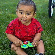 Zaiden is registered to the contest to win money with this photo: toddler, child, grass, red_shirt, toy, ladybug_toy, outdoor, sitting, curious_expression, short_hair, black_socks, green_background, cartoon_prints, baby, playtime, cute, natural_light, person, summer, casual_clothing