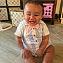 Zaiden is registered to the contest to win money with this photo: baby, child, smiling, indoor, floor, clothing, bow_tie, furniture, storage_bins, wooden_floor, happy, sitting, person, toddler, cute, room, cabinet, pink, striped, playful