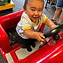 Zaiden joined the competition — help win amazing prizes! toddler, child, toy_car, steering_wheel, indoor, play_area, carpet, smiling, happy, person, shorts, legs, stroller, black_socks, red, clothing, fun, play, cute, joy
