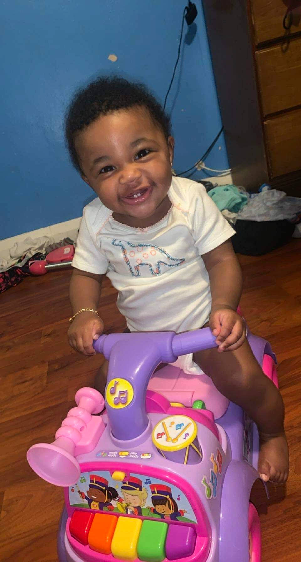 Camilla is registered to the contest to win money with this photo: baby, baby_playing_with_toys, baby_toddler_clothing, cheek, eye, finger, fun, happy, head, iris, joy, mouth, nose, person, pink, purple, riding_toy, skin, smile, standing