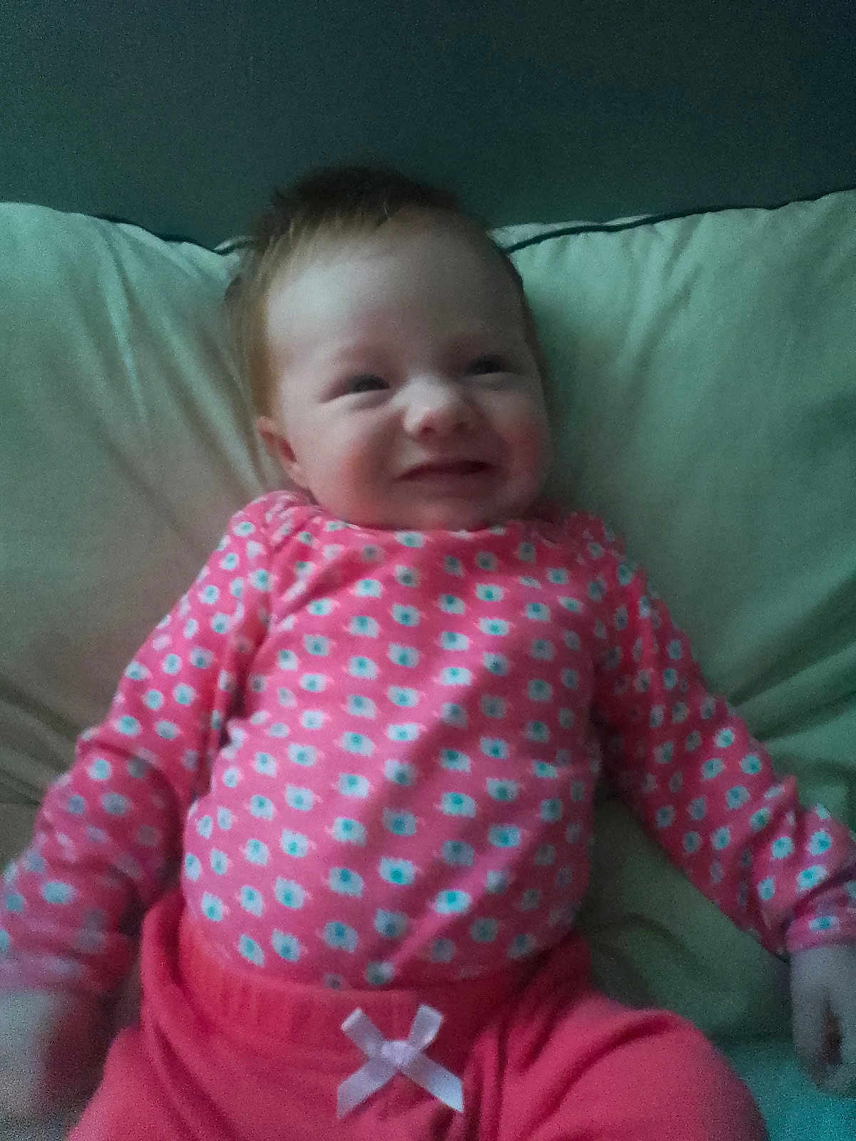 Arissa joined the competition — help win amazing prizes! baby, infant, smile, pink_clothing, bow, pillow, lying_down, happy, cute, child, face, patterned_clothing, indoors, person, young_child, soft_lighting, cozy, head, hand, sleeve