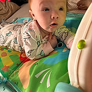 Arissa is registered to the contest to win money with this photo: baby, bed, blanket, child, closeup, colorful, comfort, curious, cute, expression, face, hands, indoor, infant, pajamas, person, play_mat, resting, toy, young_child