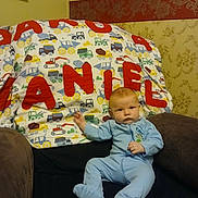 Dakota joined the competition — help win amazing prizes! baby, infant, onesie, chair, blanket, construction_vehicles, red_letters, wallpaper, indoor, furniture, child, person, cute, seated, portrait, home, cozy, soft_toys, colorful, relaxed