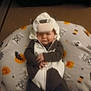 baby, child, costume, cow_costume, halloween, blanket, pumpkins, bats, spooky, sleepy, infant, cute, festive, indoors, soft, clothing, person, resting, headwear, holiday
