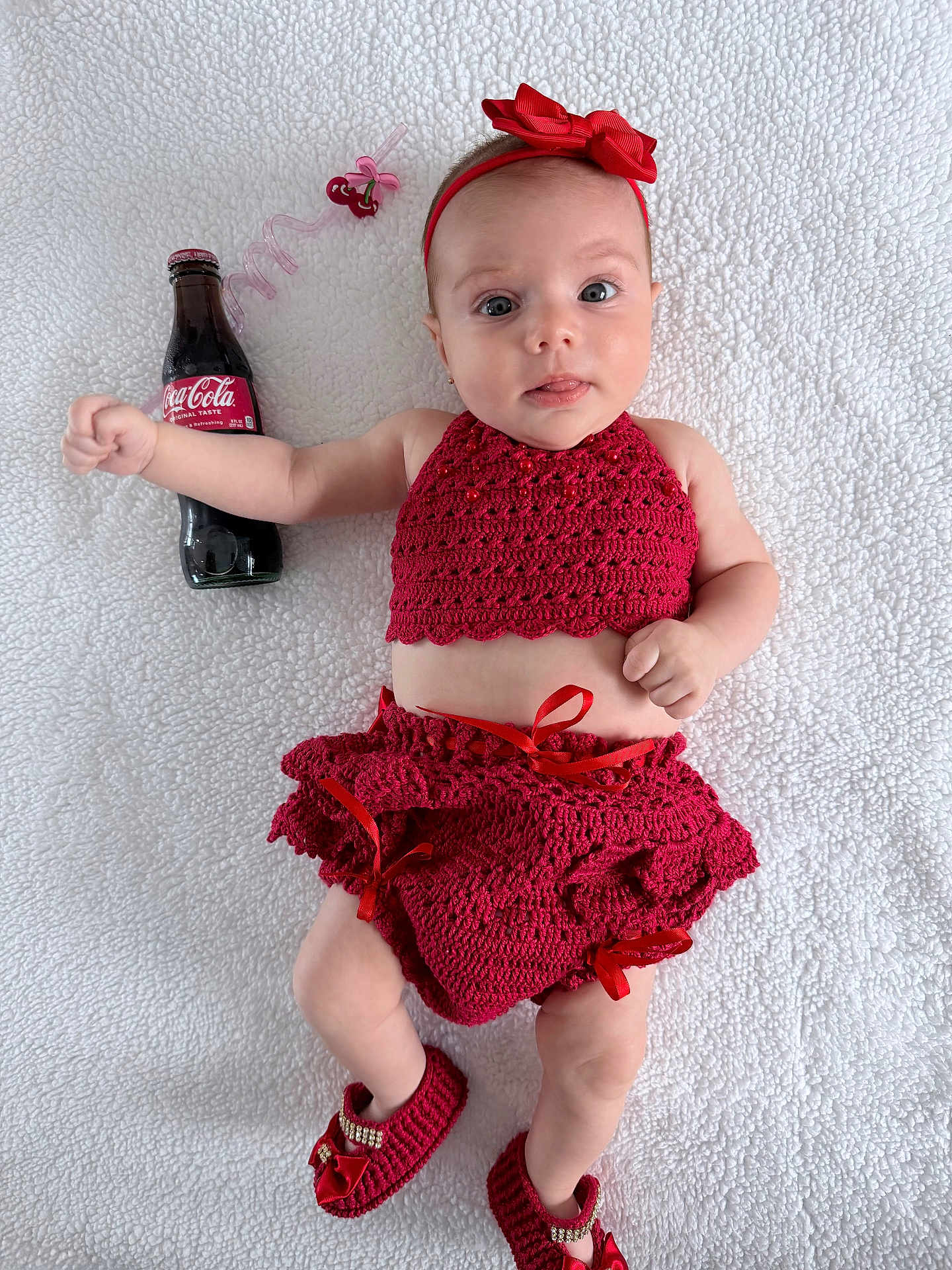 Luna is registered to the contest to win money with this photo: baby, infant, red_clothing, crochet, headband, shoes, coca_cola_bottle, straw, blanket, lying_down, cute, portrait, child, drink, accessory, white_background, expression, small_hands, small_feet, indoors