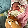 newborn, baby, blanket, plush_toy, reindeer, bed, pillow, infant, sleepy, cozy, soft, cute, wrapped, clothing, child, person, indoors, resting, cute_expression, comfort