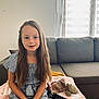 Maëlys a rejoint le concours — aidez-le/la à gagner de superbes lots ! child, girl, long_hair, striped_dress, sitting, couch, blanket, plush_toy, remote_control, indoor, window, curtains, natural_light, smile, hands, furniture, home, relaxed, portrait, young
