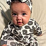 baby, child, infant, face, headband, onesie, patterned_clothing, sitting, cute, portrait, indoor, soft_lighting, smiling, young_child, happy, person, curious, baby_girl, comfort, clothing