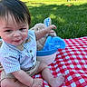 baby, barefoot, basket, beige_shorts, blue_shirt, bow_tie, child, cute, grass, infant, outdoor, park, person_walking, picnic_blanket, plush_toy, red_white_checkered, sitting, smiling, sunlight, trees