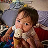 toddler, child, ice_cream, cone, indoor, blanket, cushion, person, hand, food, snack, happy, cute, face, hair, clothing, window, wall, sitting, playful