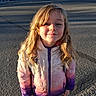 asphalt, blonde_hair, casual_clothing, child, daylight, girl, happy, jacket, outdoor, person, portrait, shadow, smile, standing, street, sunlight, urban, warm_clothing, winter, young_child