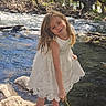 child, girl, white_dress, barefoot, stick, river, stream, rocks, trees, nature, outdoor, sunlight, water, smile, playful, summer, adventure, greenery, young, happy