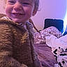 Loyal is registered to the contest to win money with this photo: toddler, child, smile, happy, indoor, cozy, sweater, face, portrait, bed, blanket, pillow, curly_hair, person, young_child, warm_clothing, lighting, expression, cute, closeup