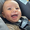 baby, child, infant, smiling, happy, laughing, portrait, face, eyes, tongue, car_seat, safety_harness, vehicle, automobile, interior, warning_label, seatbelt, travel, indoors, close_up