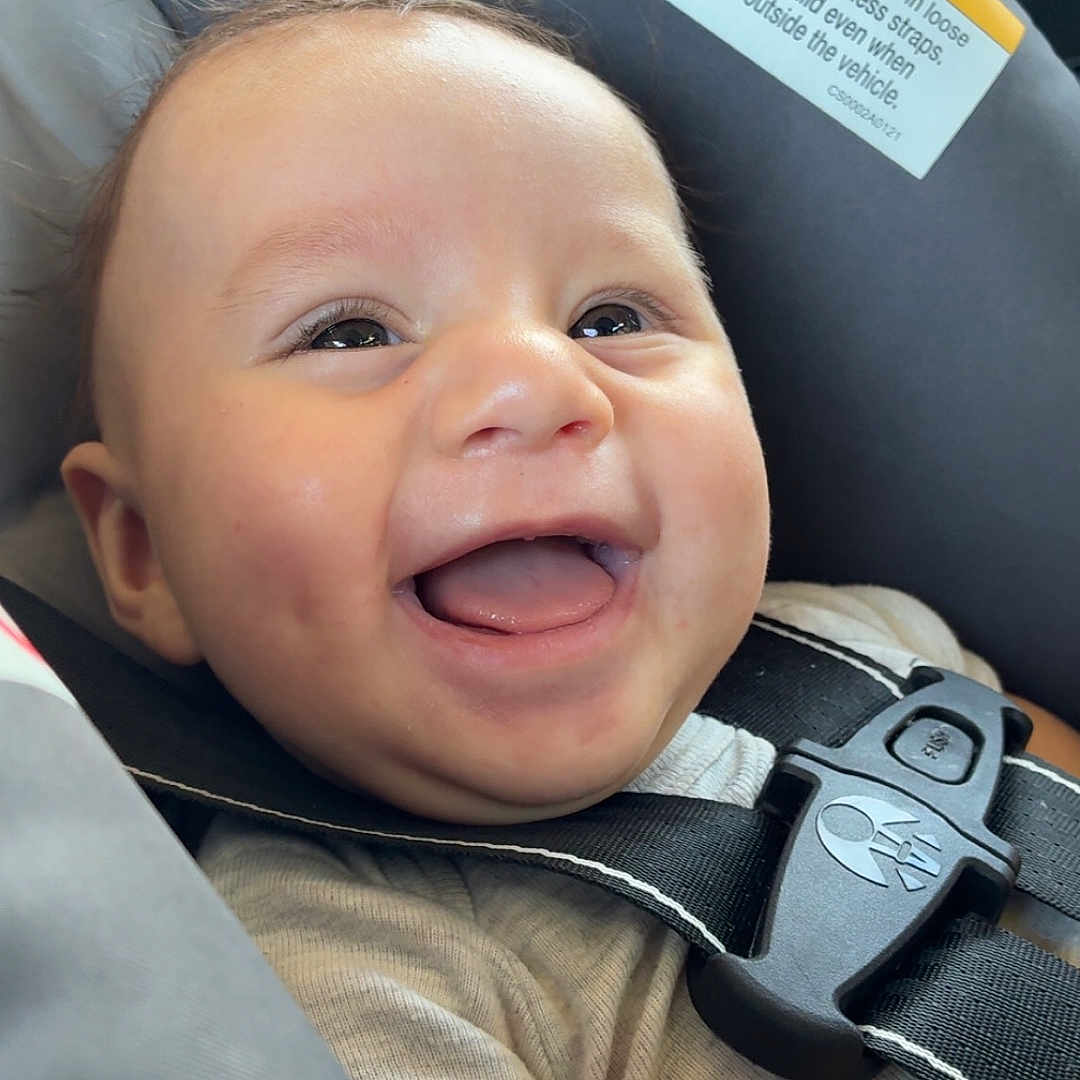 Gabriel joined the competition — help win amazing prizes! baby, child, infant, smiling, happy, laughing, portrait, face, eyes, tongue, car_seat, safety_harness, vehicle, automobile, interior, warning_label, seatbelt, travel, indoors, close_up