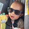 Gabriel is registered to the contest to win money with this photo: baby, infant, child, sunglasses, car_seat, safety_harness, plush_toy, giraffe, blanket, toy, vehicle, portrait, smiling, sitting, indoors, travel, colorful, close_up, playful, family